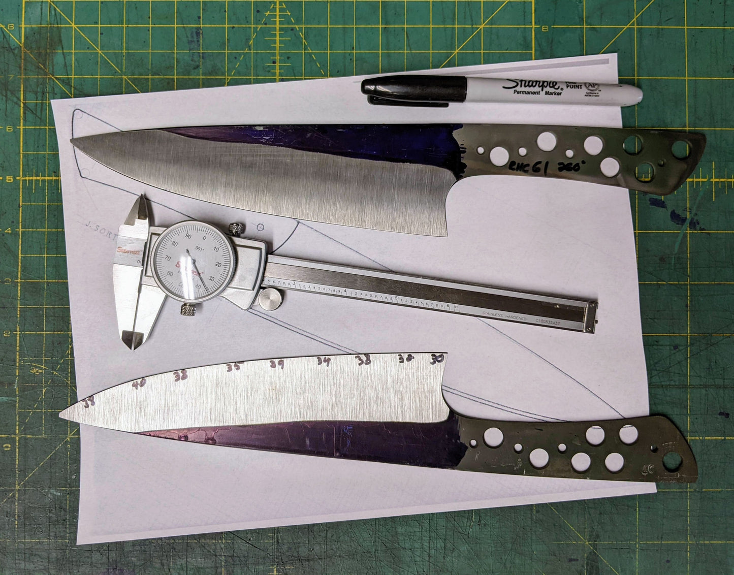 two kitchen knives under construction. A dial caliper, pen and drawing of a knife on a green background