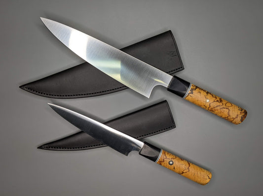 two kitchen knives and black leather sheaths on a gray background.