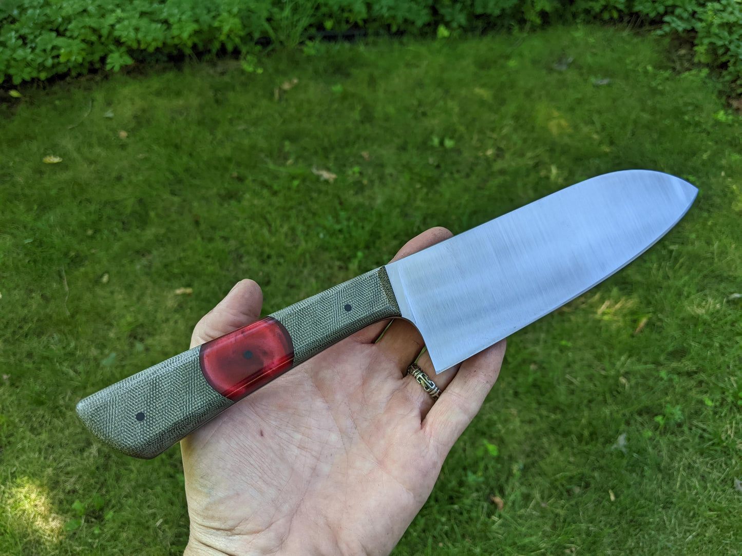 7 inch Santoku with green and red handle, handheld over a grass background