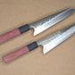 Two Japanese-style kitchen knives with patterned steel blades and red linen Micarta handles, displayed diagonally on a textured tan background.