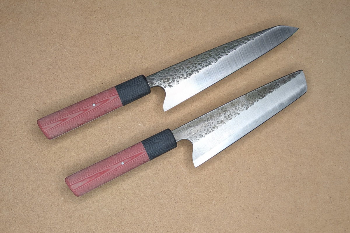 Two Japanese-style kitchen knives with patterned steel blades and red linen Micarta handles, displayed diagonally on a textured tan background.