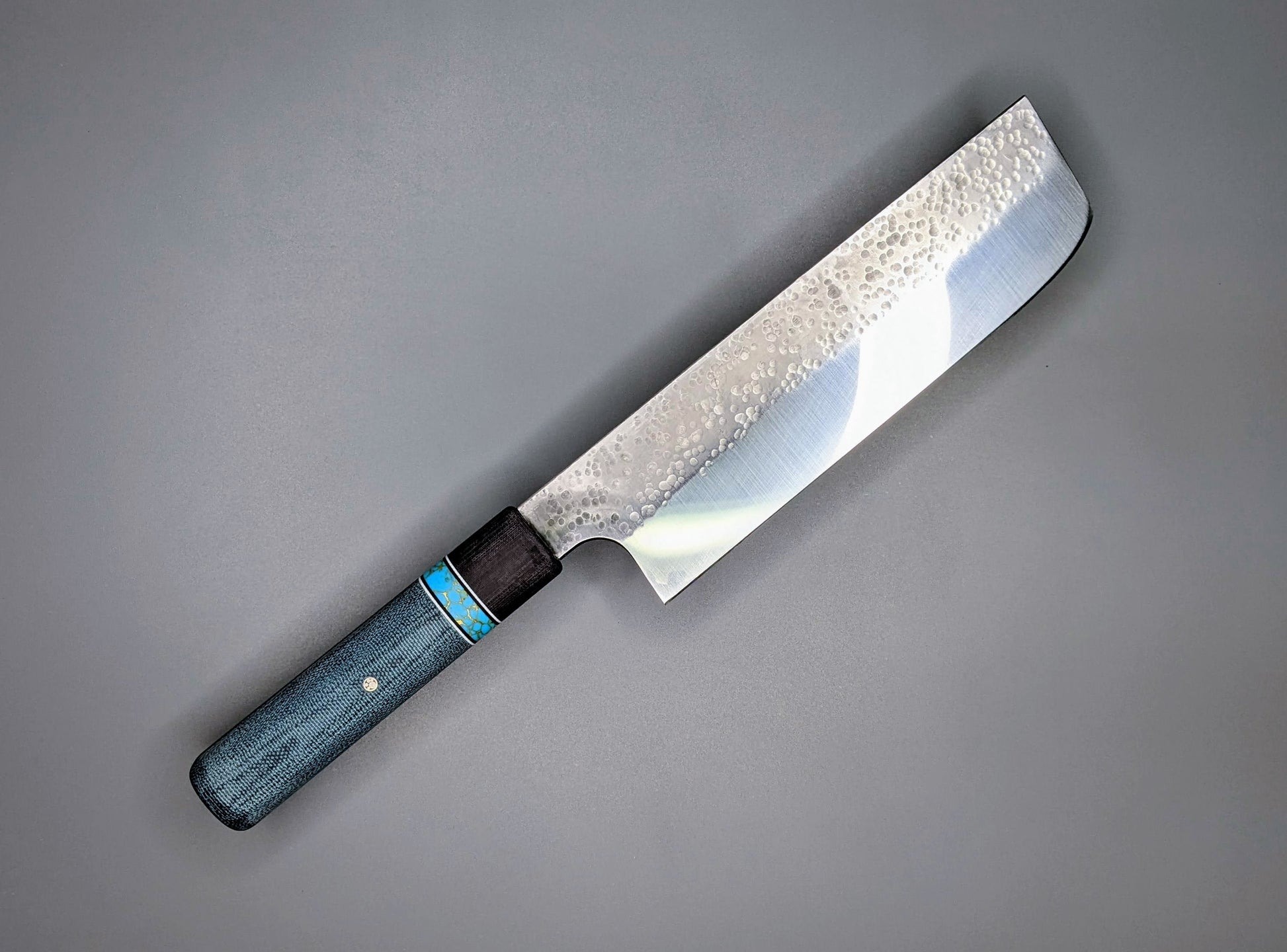 Japanese style Nakiri with a thick spine and blue handle on a gray background.