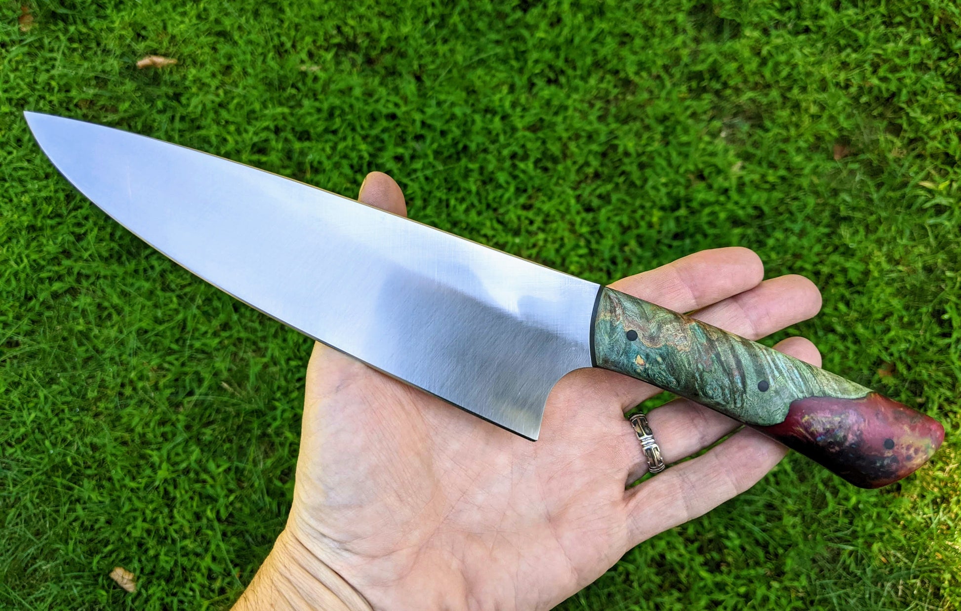 chef knife with dyed wood and resin handles on grass background
