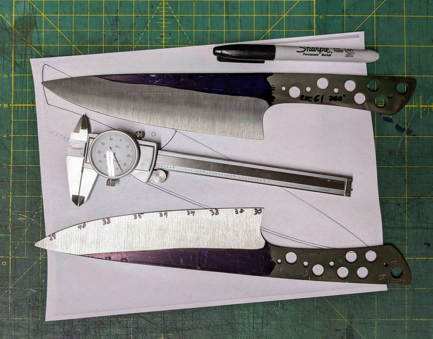 two kitchen knives under construction. A dial caliper, pen and drawing of a knife on a green background 