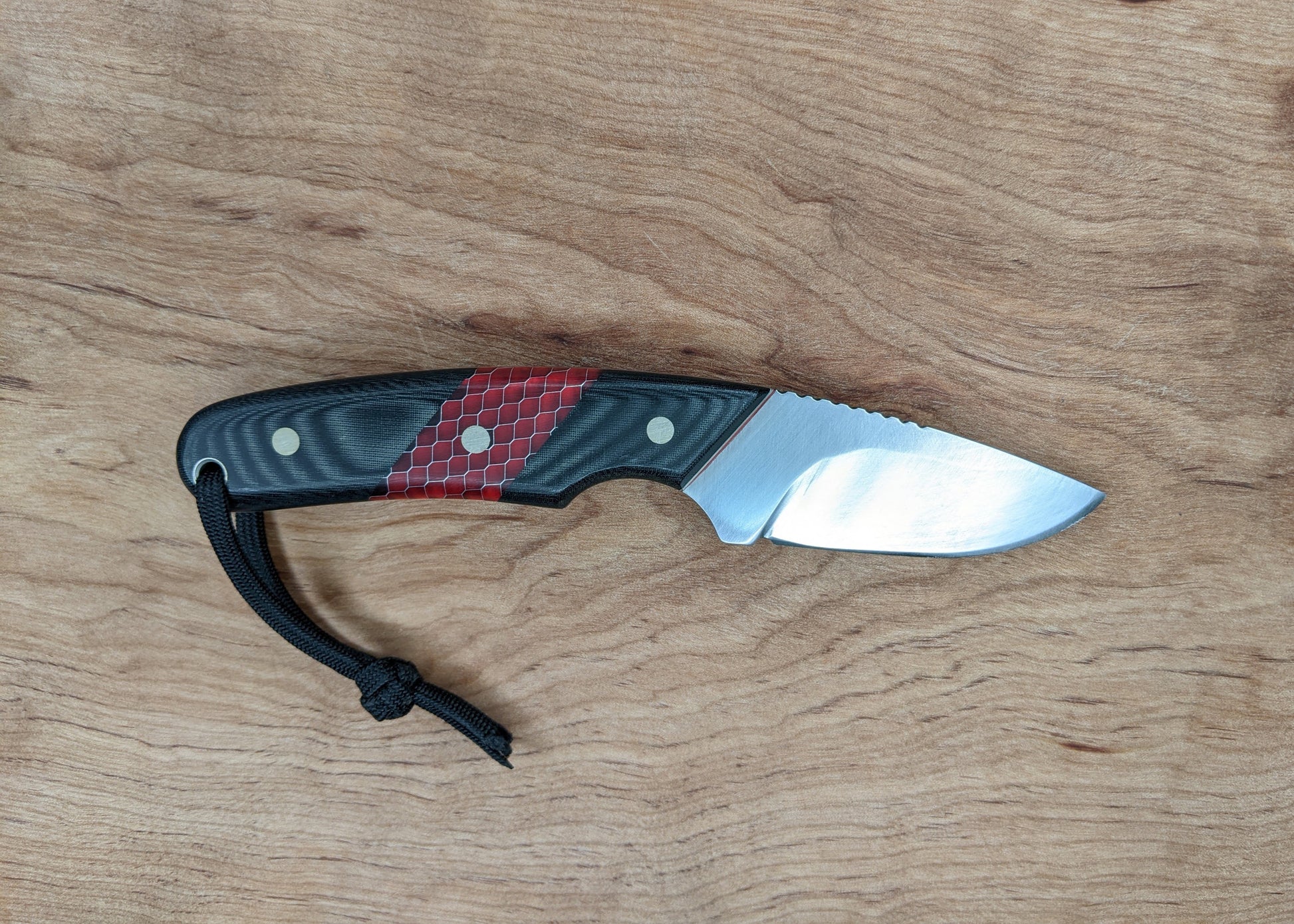 small knife with black and red handle on wooden background