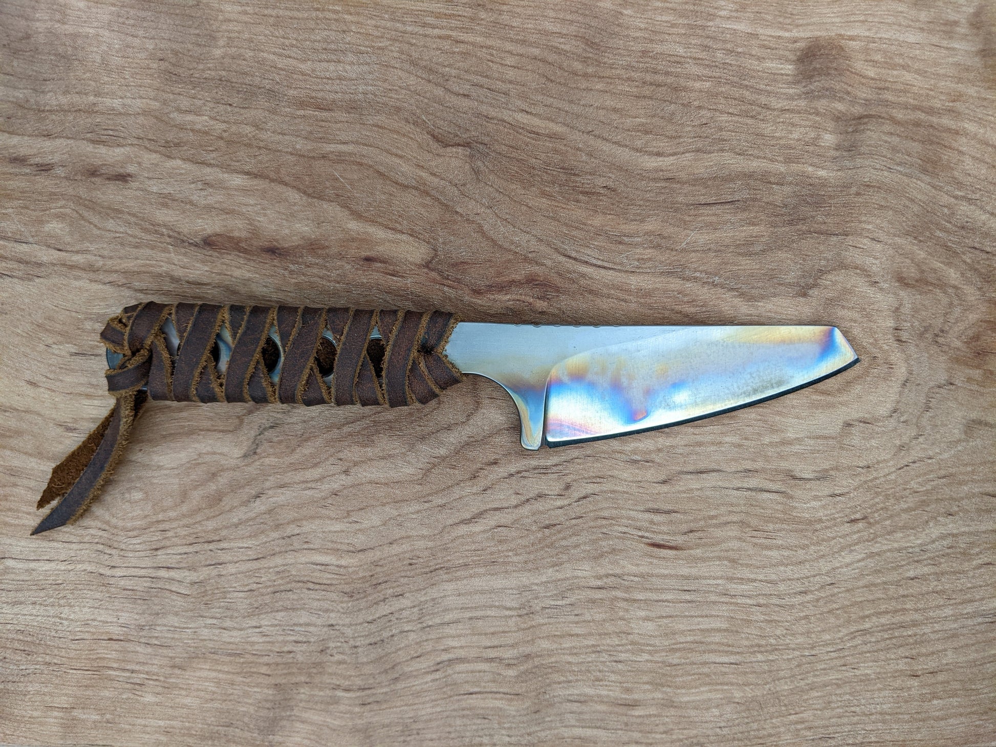 small knife with heat-treating colors and leather wrapped handle on a wooden background