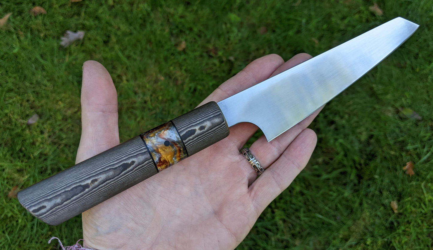 small Japanese kitchen knife handheld over grass backround